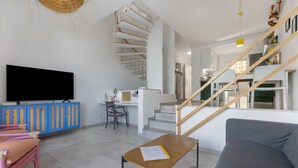 Una sala moderna con un televisor de pantalla plana, un sofá, una mesa con un libro, una escalera y un comedor.
