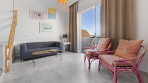Una sala moderna con un sofá, un sillón rosa, una escalera de madera y obras de arte en la pared.