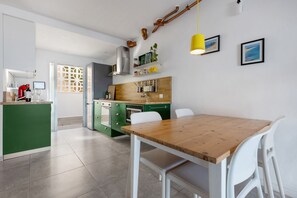 Une cuisine moderne avec une table en bois, des chaises blanches et des meubles de rangement verts.