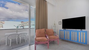 Un balcón con una mesa y sillas blancas, una silla rosa, un mueble azul y un televisor en la pared.