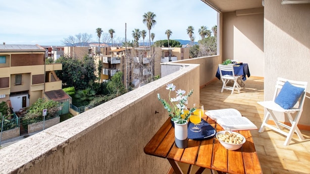 Ein Balkon mit Holztisch, Stühlen und Blick auf benachbarte Gebäude und Palmen.