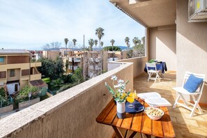 Ein Balkon mit Holztisch, Stühlen und Blick auf benachbarte Gebäude und Palmen.