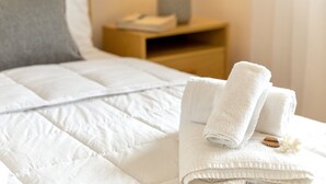 Ein ordentlich bezogenes Bett mit weißen Leinen und einem gefalteten Handtuch daneben.