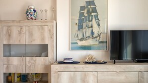 Ein Holzschrank mit Glastüren, ein gerahmtes Gemälde eines Segelschiffs und ein Flachbildfernseher auf einem Holzständer.