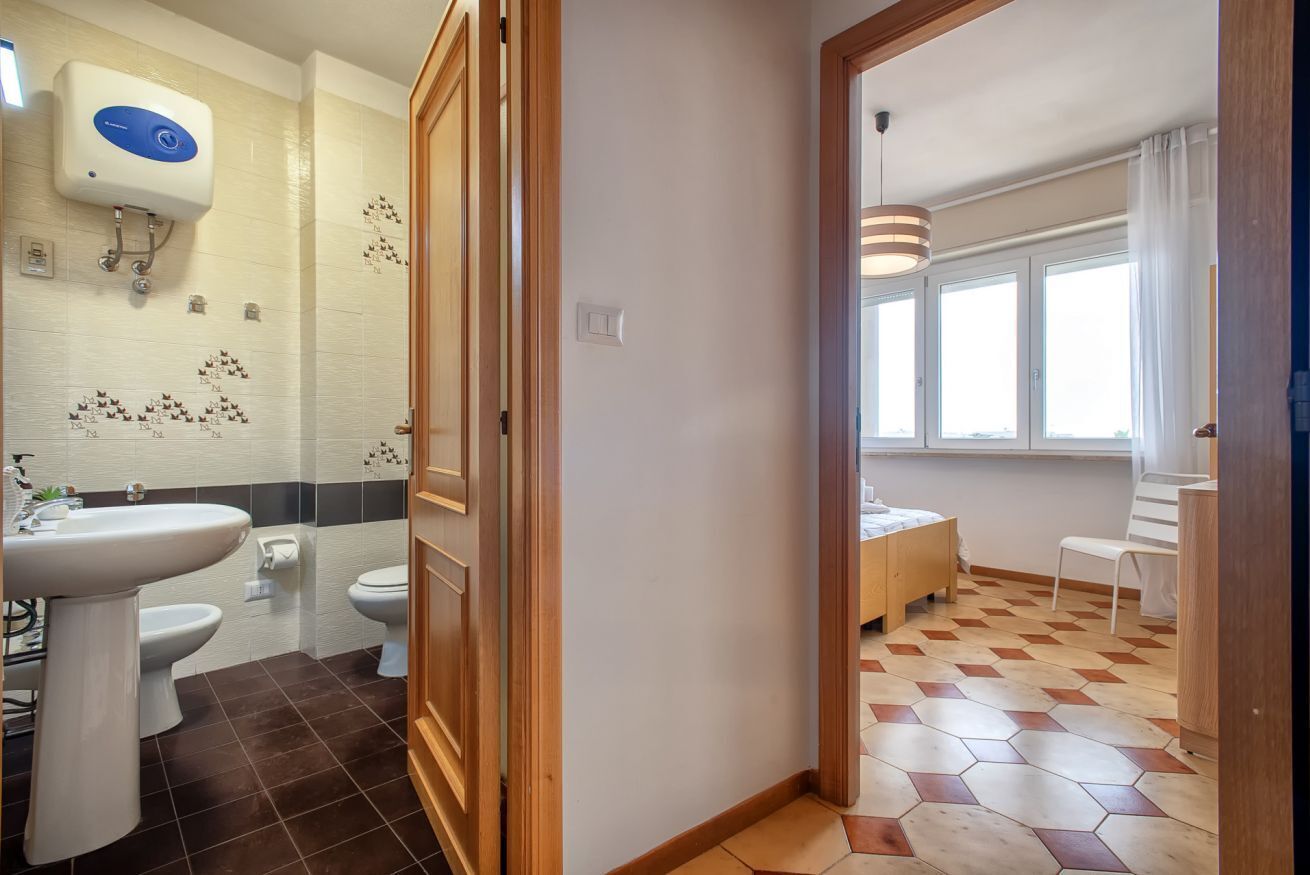 A bathroom with a sink, toilet, and shower. There is a wooden door leading to another room.