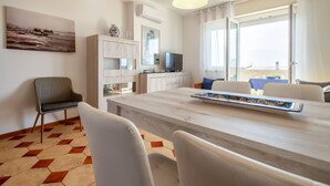 Ein modernes Wohnzimmer mit Essbereich, einer Couch, einem Fernseher und Blick ins Freie.