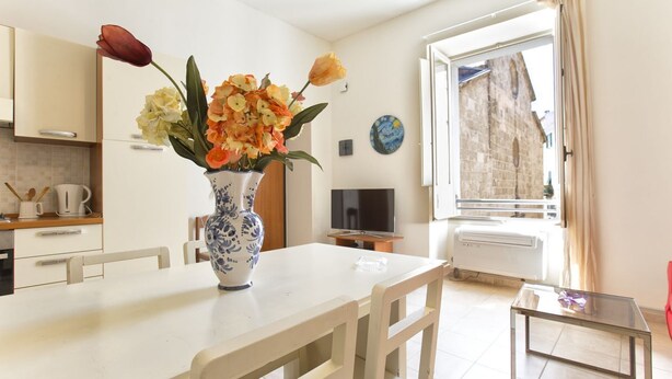 Une cuisine avec des meubles blancs, une table à manger blanche et un vase rempli de fleurs.