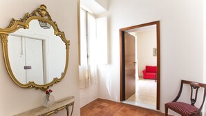 Un couloir avec un grand miroir décoratif, une chaise en bois et un canapé rouge à l’arrière-plan.