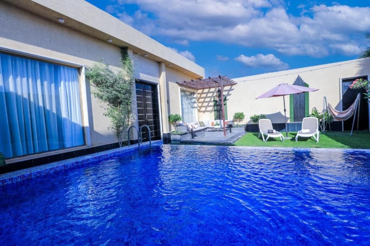 A swimming pool with a clear blue water, surrounded by a patio area with lounge chairs and a pergola.