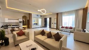 A modern living room with a sofa, armchairs, a coffee table, and a dining area with a kitchen in the background. - Lamar Park Resort  (Riyadh)