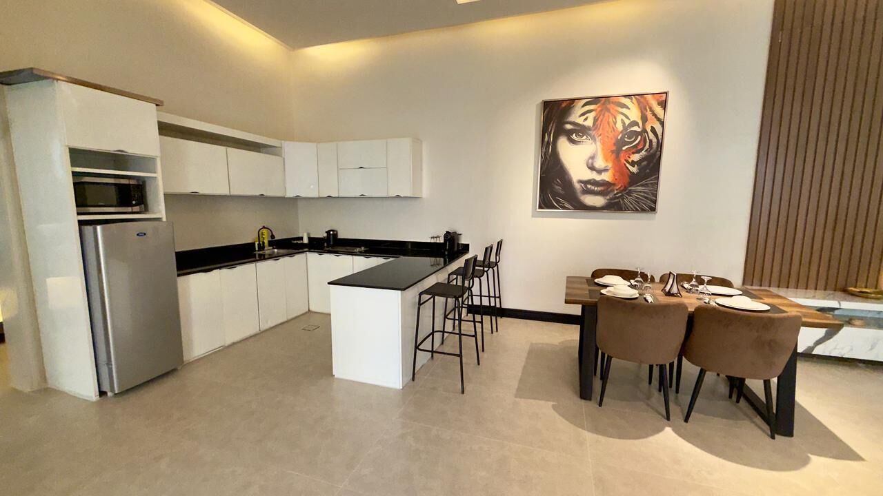 Une cuisine moderne avec des meubles blancs, un plan de travail noir et un coin repas comprenant une table et des chaises.