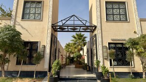 A building with two symmetrical towers, a central entrance with a decorative arch, and a paved pathway leading to the entrance. - Lamar Park Resort  (Riyadh)