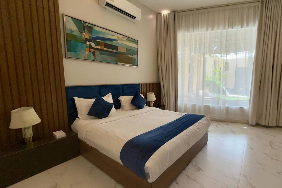 Hotelkamer met een groot bed, een schilderij aan de muur, een raam met gordijnen en een lampje op het nachtkastje.