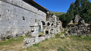 Ancient ruins with stone walls and arches, surrounded by grass and trees.