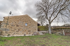 Un bâtiment en pierre avec une antenne parabolique, un arbre et un mur de pierre.
