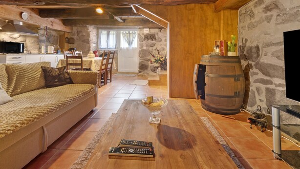 A cozy living room with a sofa, wooden coffee table, stone walls, a stone fireplace, and a kitchen in the background.
