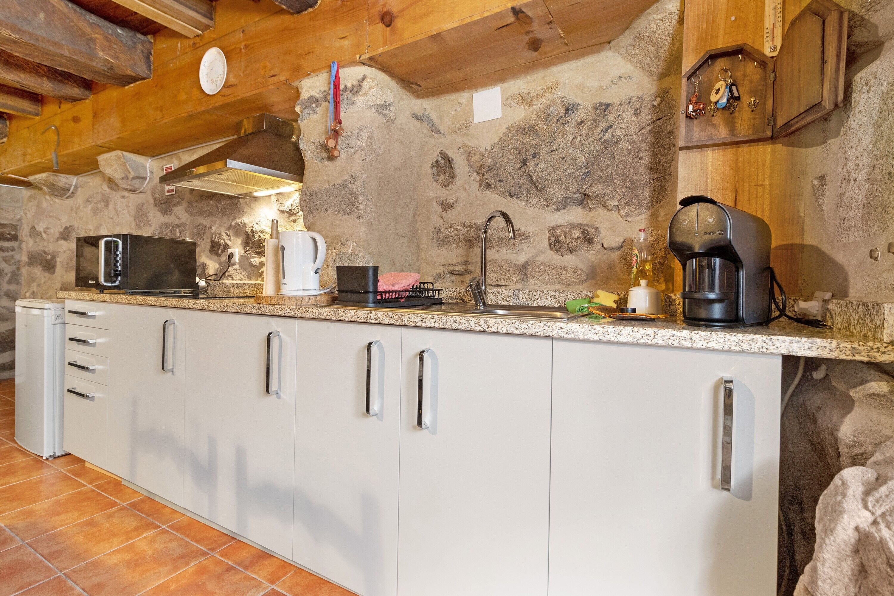 Una cocina con pared de piedra, microondas, cafetera y lavabo.