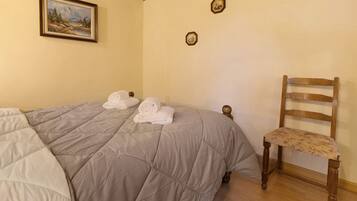 A bedroom with a bed, two framed pictures on the wall, and a wooden chair.