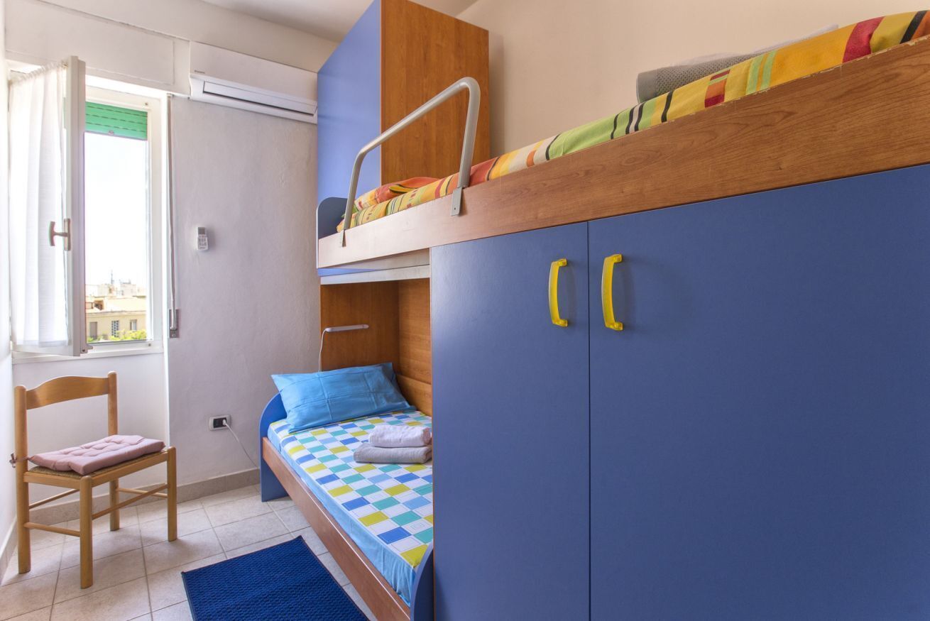 Un dormitorio con una cama litera, una cama individual, una silla de madera y un armario con pomos amarillos.