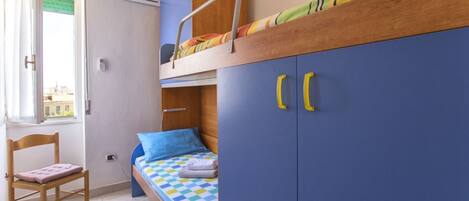 Un dormitorio con una cama litera, una cama individual, una silla de madera y un armario con pomos amarillos.