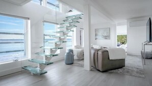 A modern interior with a glass staircase, a sofa, and a view of the sea. - Vashon Modern Waterfront Retreat+Private Beach+BBQ+Firepit (Vashon)