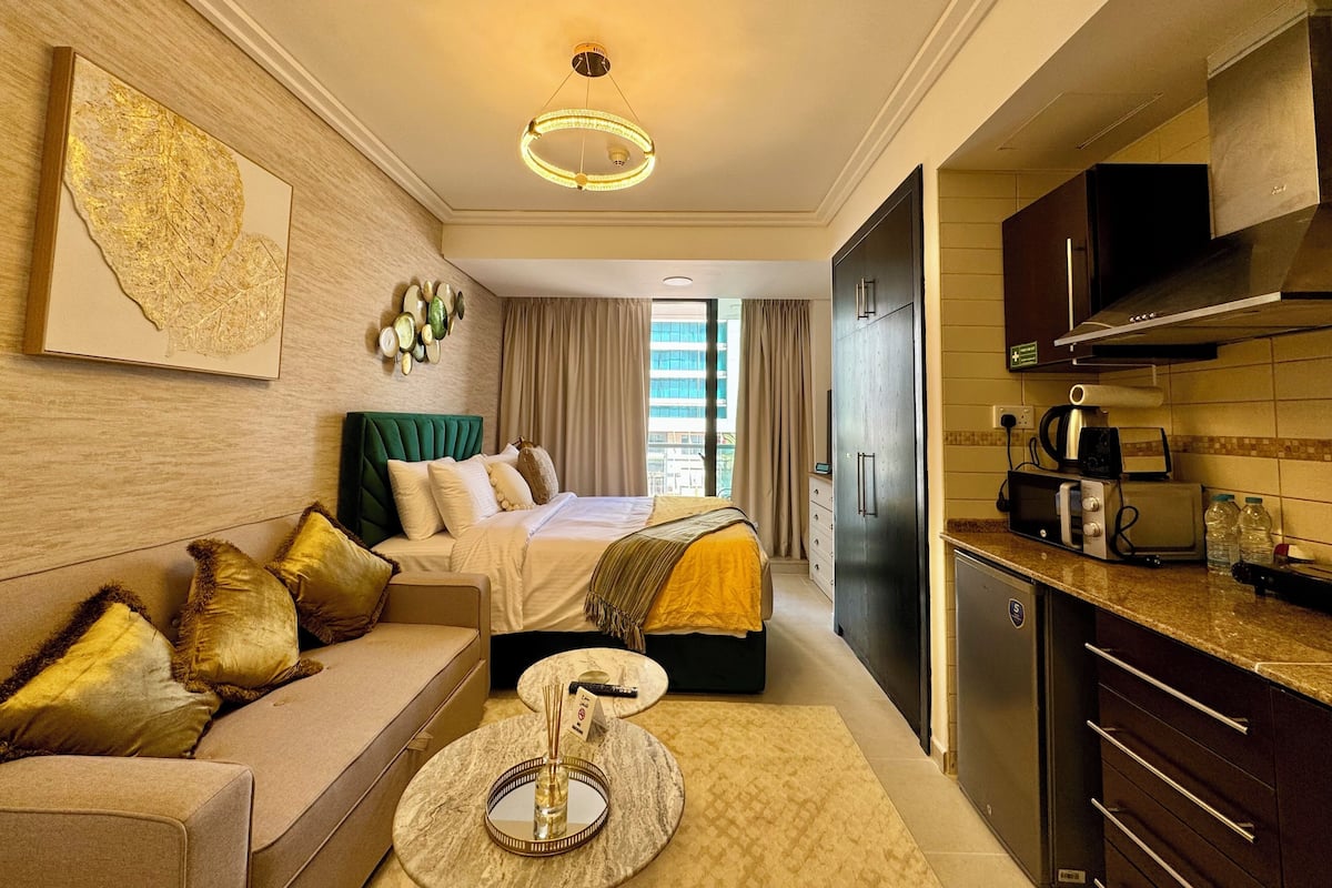Une chambre d’hôtel comprenant un lit, un canapé, une petite table ronde avec un vase, un coin cuisine équipé d’un four à micro-ondes, d’un grille-pain et de placards.