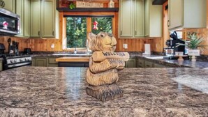 A kitchen with green cabinets, a granite countertop, and a wooden bear sculpture with "WELCOME" on it. - Eagle River Clover Pines Holiday Home (Eagle River)