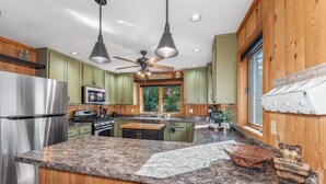 A kitchen with granite countertops, wooden cabinets, a stainless steel refrigerator, a microwave, and a ceiling fan. - Eagle River Clover Pines Holiday Home (Eagle River)