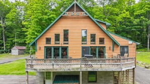 A two-story log cabin with a balcony and a small porch. - TB-19 Thunder Bay Resort Cabin 19 (Phelps)
