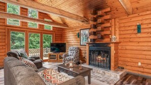 A log cabin interior with a fireplace, a sofa set, a television, and large windows. - TB-19 Thunder Bay Resort Cabin 19 (Phelps)