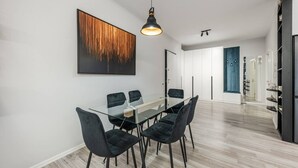 Een moderne eethoek met een glazen tafel en zwarte stoelen, een groot abstract schilderij aan de muur en een hanglamp erboven.