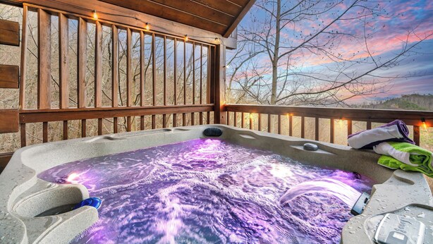 Un jacuzzi con terraza de madera y vistas a árboles y un atardecer.