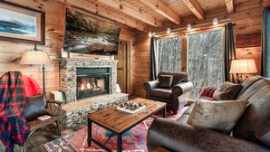 Un interior de cabaña acogedor, con chimenea de piedra, mobiliario de cuero y ventanas amplias.