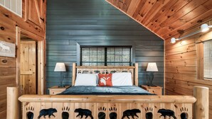 Dormitorio de cabaña de madera con cama, dos mesitas de noche, una ventana y un cabecero de madera con huellas de animales.