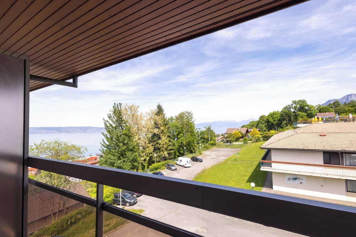 A balcony with a view of a parking lot, a grassy area, and a building with a tiled roof.