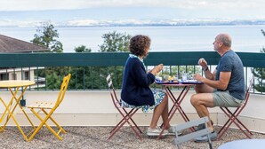 Zwei Personen essen an einem Tisch im Freien mit Blick auf ein Gewässer und entferntes Land.