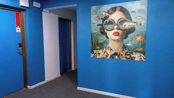 A hallway with blue walls, a door with a red sign, and a large mural of a woman with fish.