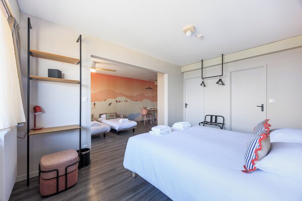 A hotel room with a bed, two bedside tables, a desk, a chair, a small stool, and a wall with a mural.