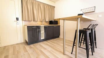 Een kleine keuken met een houten aanrecht, een ingebouwde oven en een spoelbak. Twee zwarte krukken en een metalen tafelje staan er.