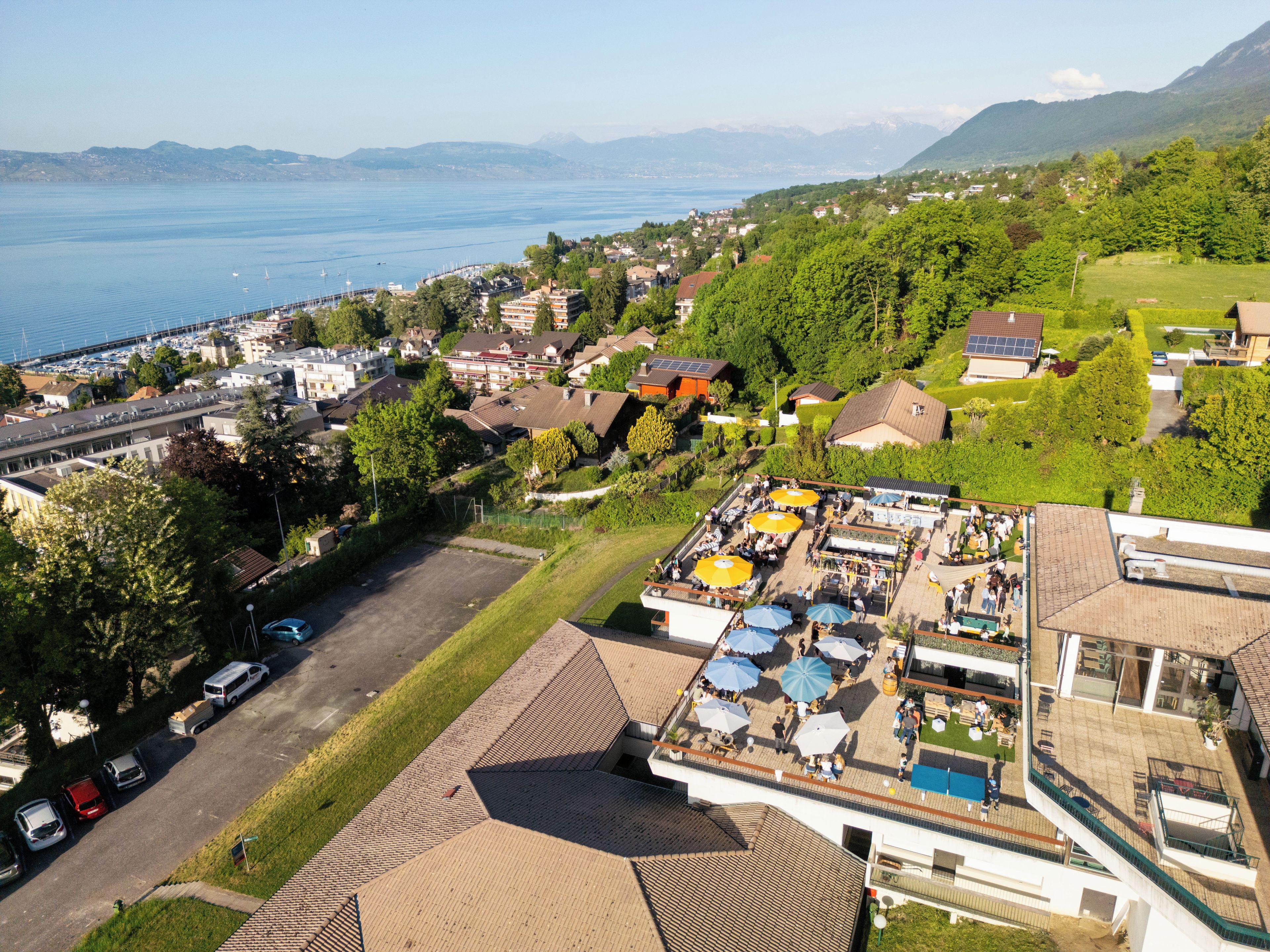 An aerial view of a coastal town with a marina, residential buildings, and a rooftop bar with umbrellas.
