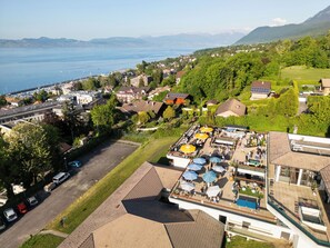 En vy över en kuststad från ovan, med en småbåtshamn, bostadshus och en bar på taket med parasoller.