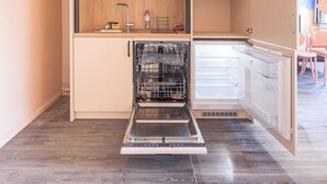 A compact kitchen with a dishwasher, microwave, and a small sink. - Côté Lac Hostel (Neuvecelle)