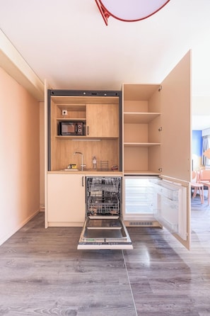 A compact kitchen with a dishwasher, microwave, and a small sink. - Côté Lac Hostel (Neuvecelle)
