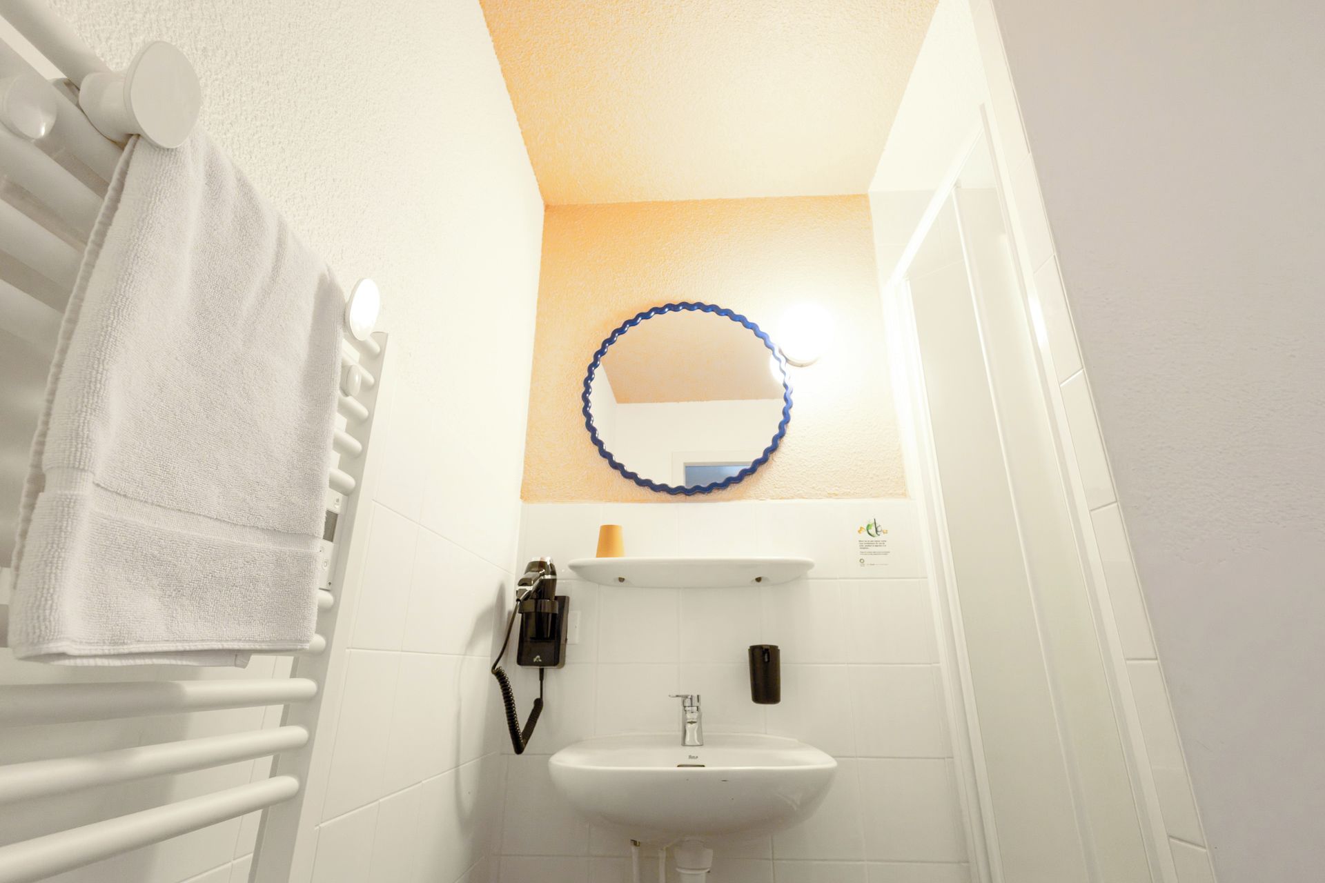 Une petite salle de bain avec un lavabo blanc, un porte-serviettes et un miroir doté d’un cadre bleu.