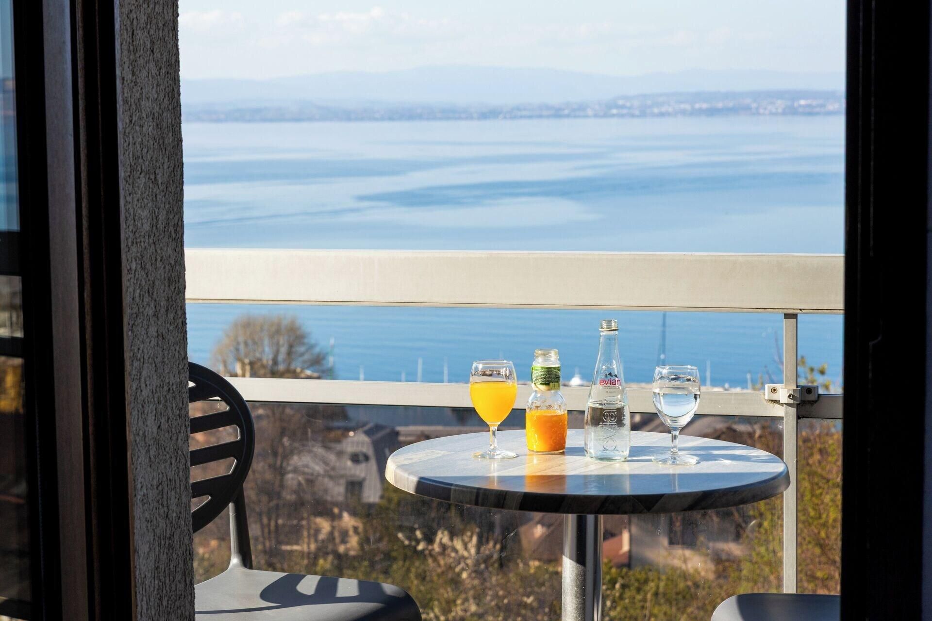 Une table avec des boissons et une bouteille sur un balcon donnant sur une étendue d’eau.