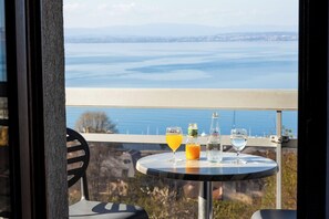 A table with drinks and a bottle on a balcony overlooking a body of water. - Côté Lac Hostel (Neuvecelle)
