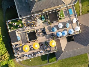 Vista aérea de un patio con asientos al aire libre, sombrillas y una piscina.