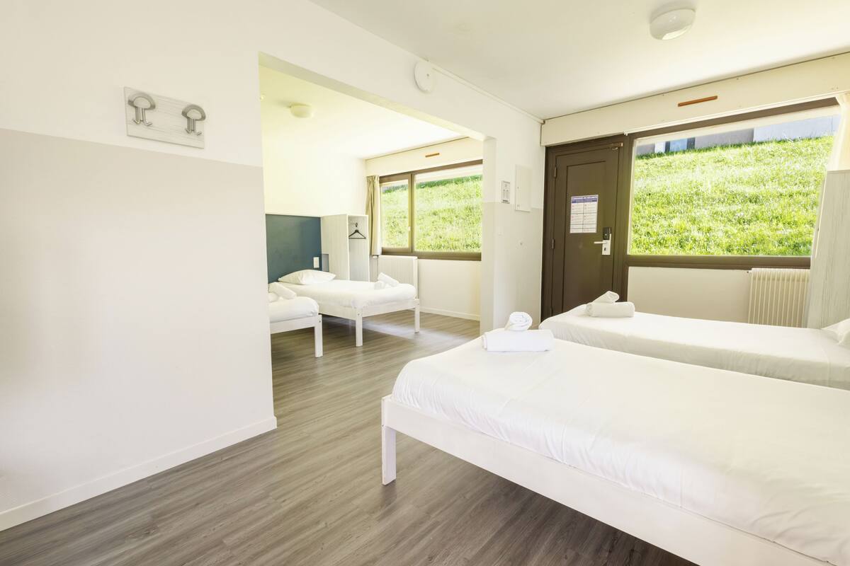 A hotel room with two beds, a sitting area, and a window with a view of greenery.