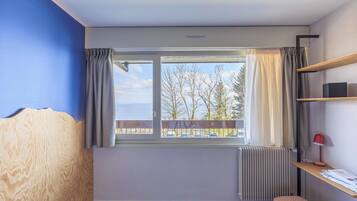 A room with a window, a radiator, a wooden headboard, a bench, and a shelf with a lamp.