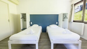 A room with two single beds, a blue accent wall, a window with a view, and a radiator. - Côté Lac Hostel (Neuvecelle)
